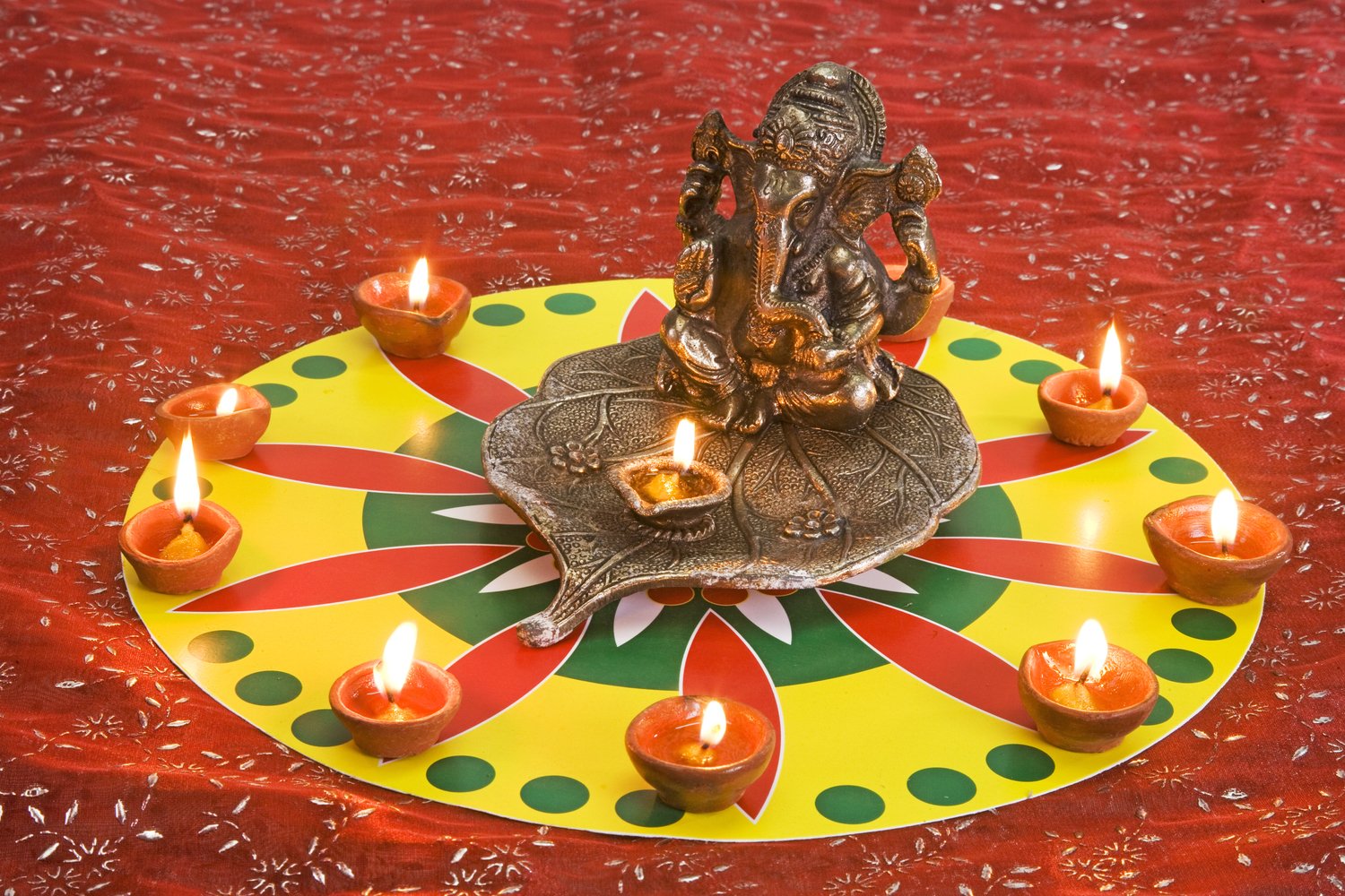 A Ganesha statue surrounded by lit diyas on a rangoli-style design.